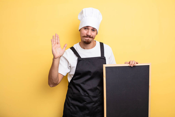 chef man smiling happily, waving hand, welcoming and greeting you - Φωτογραφία, εικόνα