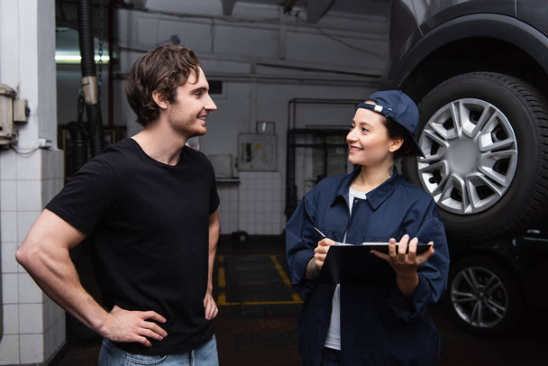 Θετικός οδηγός στέκεται κοντά εργαζόμενη με πρόχειρο κοντά στο αυτοκίνητο σε υπηρεσία  - Φωτογραφία, εικόνα