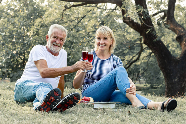 Couple elderly were drinking together on the anniversary celebration of love. Couple seniors sipping wine fruity together with happy face in the park. Concept of an elderly lover. - Фото, зображення