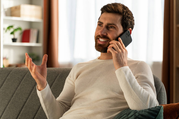 Bearded guy wearing glasses smiling to the camera and having conversation at his smartphone. Stock photo - Valokuva, kuva