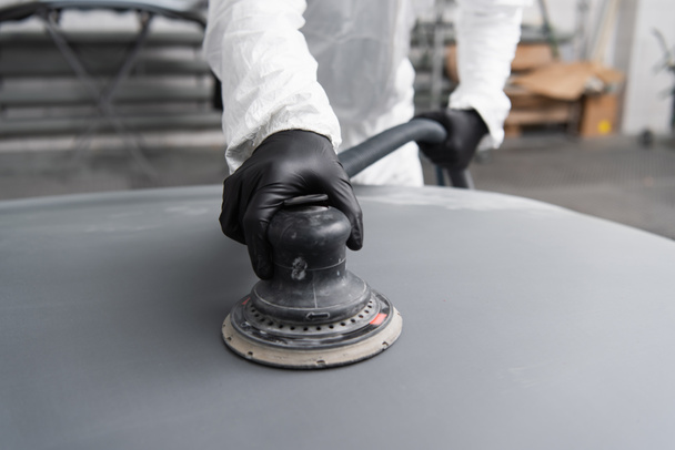 Cropped view of workman in gloves and hazmat suit polishing car in garage  - Фото, изображение