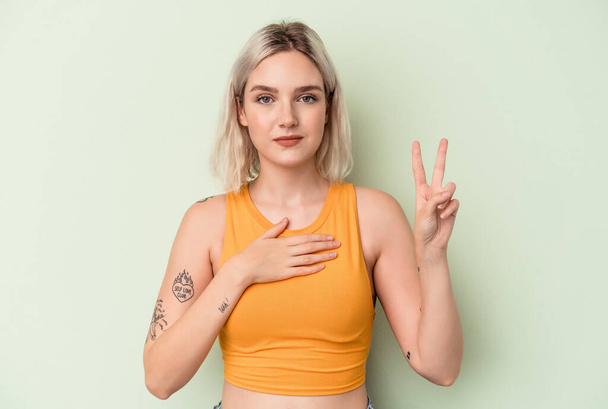Young caucasian woman isolated on green background taking an oath, putting hand on chest. - Foto, Imagem