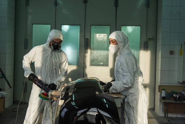 Workman in protective suit polishing car part near colleague in service  - Photo, Image