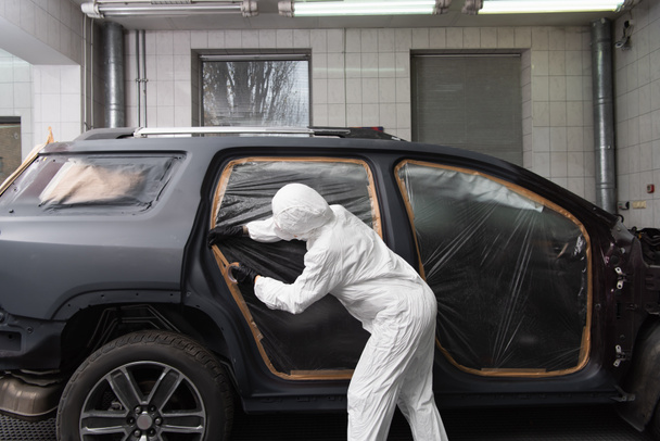 Workwoman in protective suit applying tape on car in service  - Zdjęcie, obraz