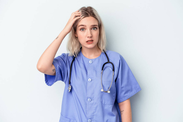 Young nurse woman isolated on blue background being shocked, she has remembered important meeting. - Φωτογραφία, εικόνα
