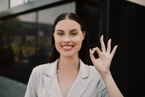 Small business owner office worker smiling happy woman standing outside building showing OK gesture sign. Female successful executive girl on the street. Copy space. - Foto, imagen