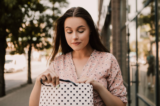 Surprised lady open and look into bags shopper woman dressed pink flower pattern dress carrying enjoying new clothes packs things after shopping buyings sales black friday concept - Fotó, kép