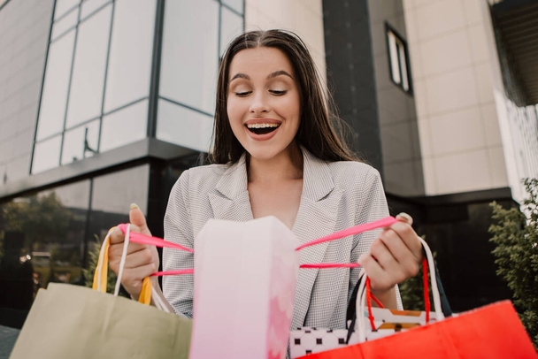 Surprised lady open and look into bags shopper woman dressed plaid blazer carrying enjoying new clothes packs things after shopping buyings sales black friday concept - Zdjęcie, obraz