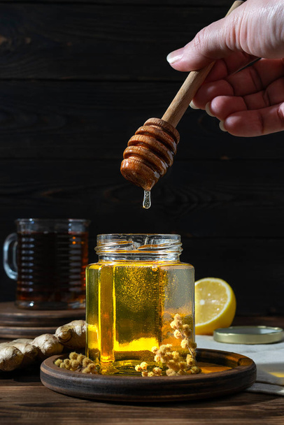 A transparent jar with golden honey on a wooden saucer - Фото, зображення