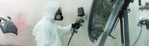 Side view of workman in protective suit and goggles coloring car part with airbrush, banner  - Photo, Image