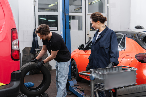 Mladí mechanici pracují s pneumatikami v blízkosti aut v garáži  - Fotografie, Obrázek