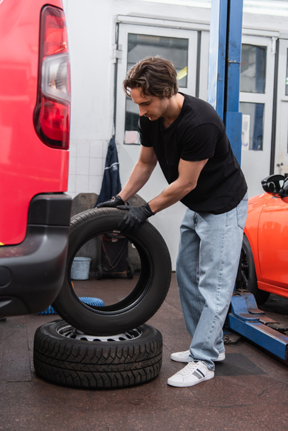 Young mechanic holding tire near cars in service  - Foto, Bild