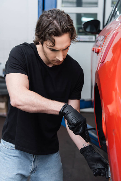 Workman in gloves working with screwdriver and car wheel in garage  - Fotó, kép