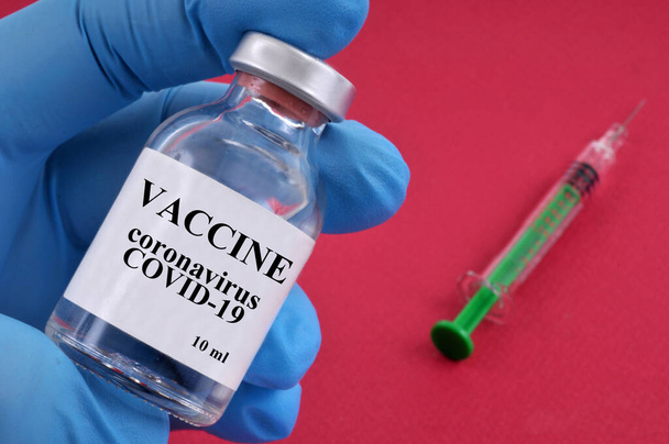 Koronavirusrokotekonsepti - injektiopullo kädessä ja ruisku punaisella pohjalla - Valokuva, kuva