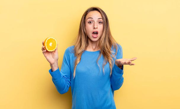 pretty woman feeling extremely shocked and surprised holding half orange - Fotoğraf, Görsel