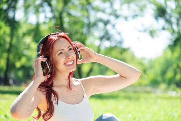 Young woman happens to have music in a summer park - Fotoğraf, Görsel