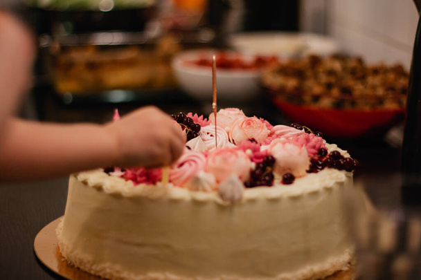 Торт на день народження з рожевими збитими вершками. Дитина кладе свічки в торт
. - Фото, зображення