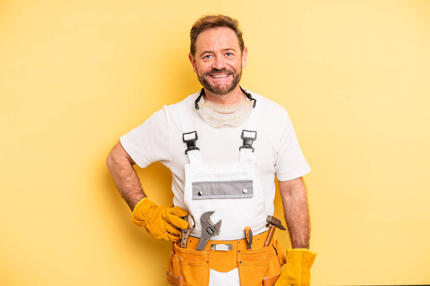 middle age man smiling happily with a hand on hip and confident. handyman and repair concept - Foto, afbeelding