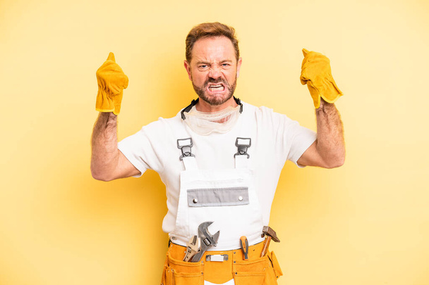 middle age man shouting aggressively with an angry expression. handyman and repair concept - Foto, afbeelding