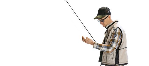Portrait of young man, professional fisherman with fishing rod, spinning and equipment going to river isolated over white studio background - 写真・画像