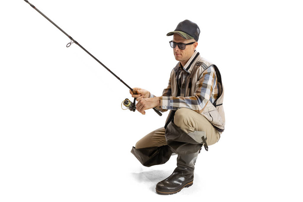 Portrait of young man, professional fisherman with fishing rod, spinning and equipment going to river isolated over white studio background - 写真・画像