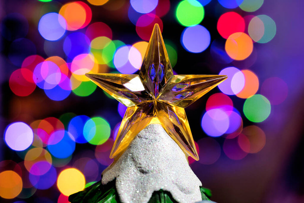 зірка у формі жовтого прозорого акрилового ялинки зверху на пластиковій дереві і кольорові вогні позаду
 - Фото, зображення