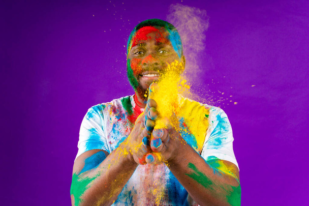 Afro Američan muž slaví holi festival ve fialovém studiu pozadí - Fotografie, Obrázek