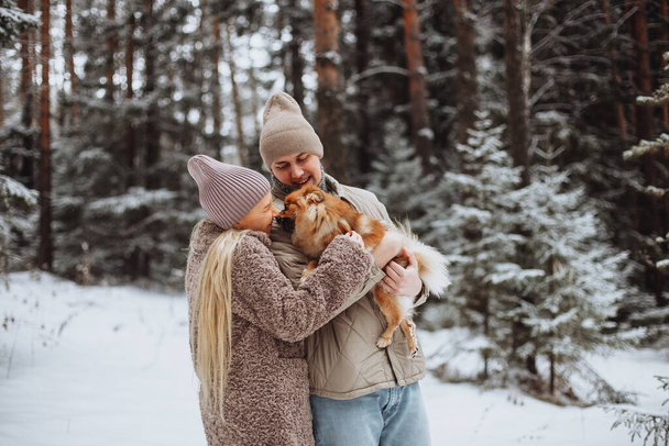 A loving couple in the winter outdoors in a snowy forest hugging. Girl in a hat and beige fur coat, a man with a beige hat and beige jacket - Photo, Image