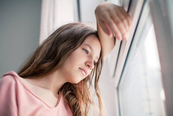 Thoughtful girl looking at window, sad depressed teenager spending time alone at home, young upset pensive woman feeling lonely or frustrated thinking about problems - Photo, Image