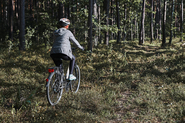Active woman cycling on forest road. Female riding bicycle off-road route on summer vacation day. Woman wearing bicycle helmet and gloves - Fotografie, Obrázek