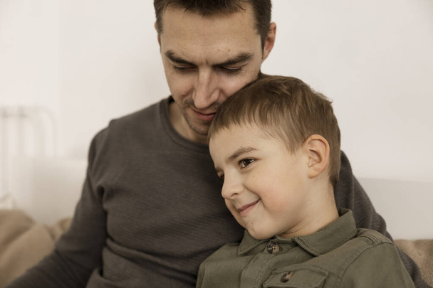 Portrait of father and his son. Dad loves his boy. Young attractive man and little caucasian kid have fun together. Interior and clothes in natural earth colors. Cozy environment. - Foto, Bild