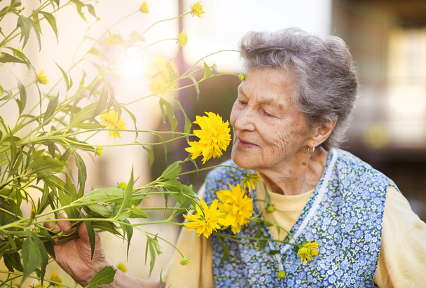 Senior woman with flower in garden - Zdjęcie, obraz