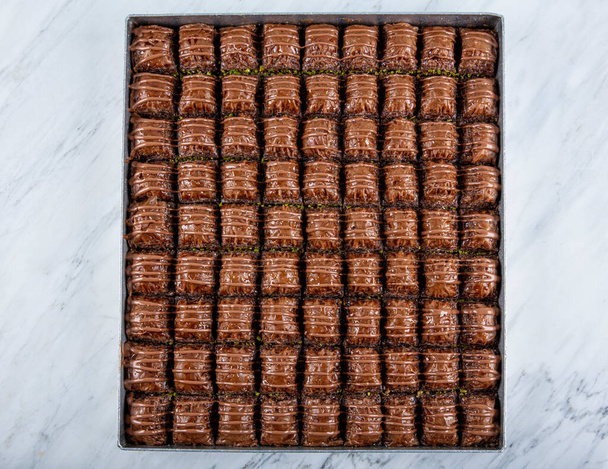 Traditional Turkish baklava. Turkish Dessert Chocolate Baklava with Pistachio Turkish name; Cikolatali Baklava. Chocolate Baklava on tray on marble floor. - Фото, зображення