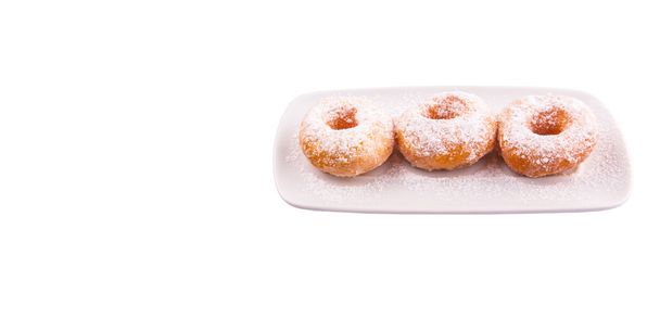 Donut caseiro com coberturas de açúcar em uma placa branca sobre fundo branco
 - Foto, Imagem
