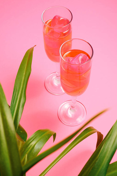 Composición retro mínima de dos copas de champán con cóctel y hojas verdes sobre fondo rosa. - Foto, Imagen