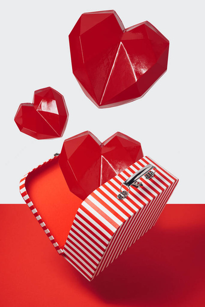 Creative layout made with geometric hearts falling out of suitcase with red and white stripes. Love concept. - Photo, Image