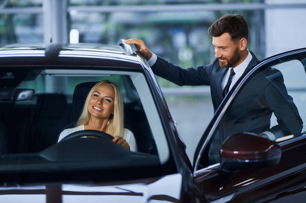 Salesman showing to female customer various auto at salon - Фото, изображение