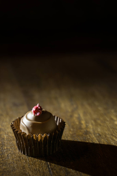 Single spot lighted rasberry toped chocolate praline on a wooden shelf - Fotó, kép