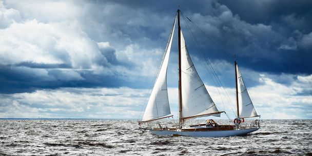 Oude dure vintage houten zeilboot (yawl) close-up, zeilen in een open zee. Dramatisch wolkenlandschap. Kust van Maine, VS - Foto, afbeelding
