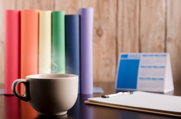 cup of coffee or tea with hot steam, books with lgtbi flag colors, on the desk. - Foto, immagini