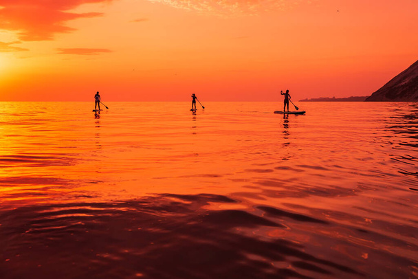 Travelers on stand up paddle board at quiet sea with sunset or sunrise. Girls on Red Paddle sup board and sunset with reflection - Foto, imagen