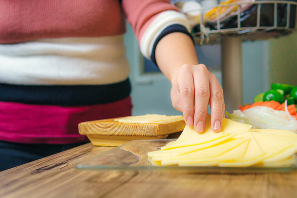 Στο τραπέζι υπάρχουν φέτες κίτρινου τυριού, το χέρι μιας γυναίκας μπορεί να δει να παίρνει μια φέτα για να το οργανώσει ή να φάει. - Φωτογραφία, εικόνα