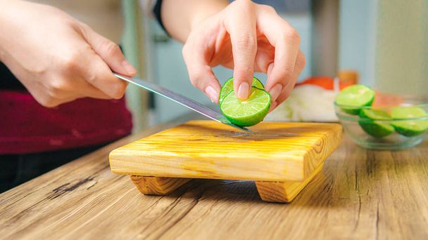 On the table is a hand with a knife cutting green lemons on a wooden board. - 写真・画像