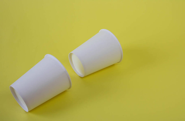 Dos tazas de papel blanco sobre un fondo amarillo. - Foto, imagen
