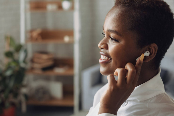 Side view of a afro american woman talking with colleagues through earphones. Close-up portrait. - Fotó, kép