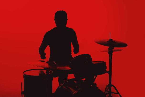 Silhouette of a young man playing drums on a red background. - Foto, Imagen
