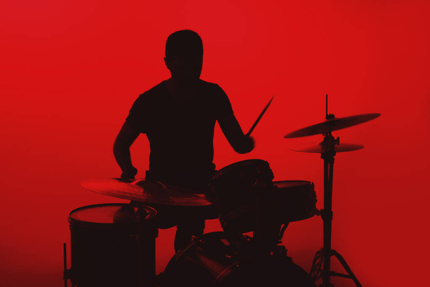 Silhouette of a young man playing drums on a red background. - Fotoğraf, Görsel