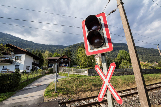 Level crossing sign, called crossbuck, saltire or Saint Andrews cross, standing on a road which crosses a railway track in Germany or austria, called bahnubergang; in german, with a barrier and traffic lights - Fotó, kép