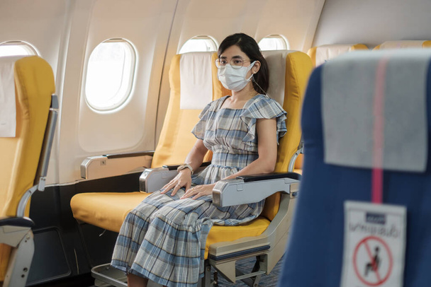 Korumalı yüz maskesi takan kadın uçakta ya da toplu taşımada oturuyor, Coronavirus hastalığı enfeksiyonunu koruyor, seyahat etmeye hazır turist. Sonraki Normal: Turizm ve Yeniden Açılış Konsepti - Fotoğraf, Görsel