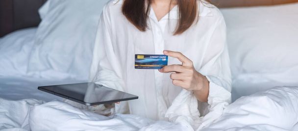 kobieta korzystająca z tabletu i karty kredytowej do zakupów online podczas składania zamówienia w łóżku rano w domu. technologia, handel elektroniczny, cyfrowa bankowość płatności online i koncepcja mieszkania - Zdjęcie, obraz